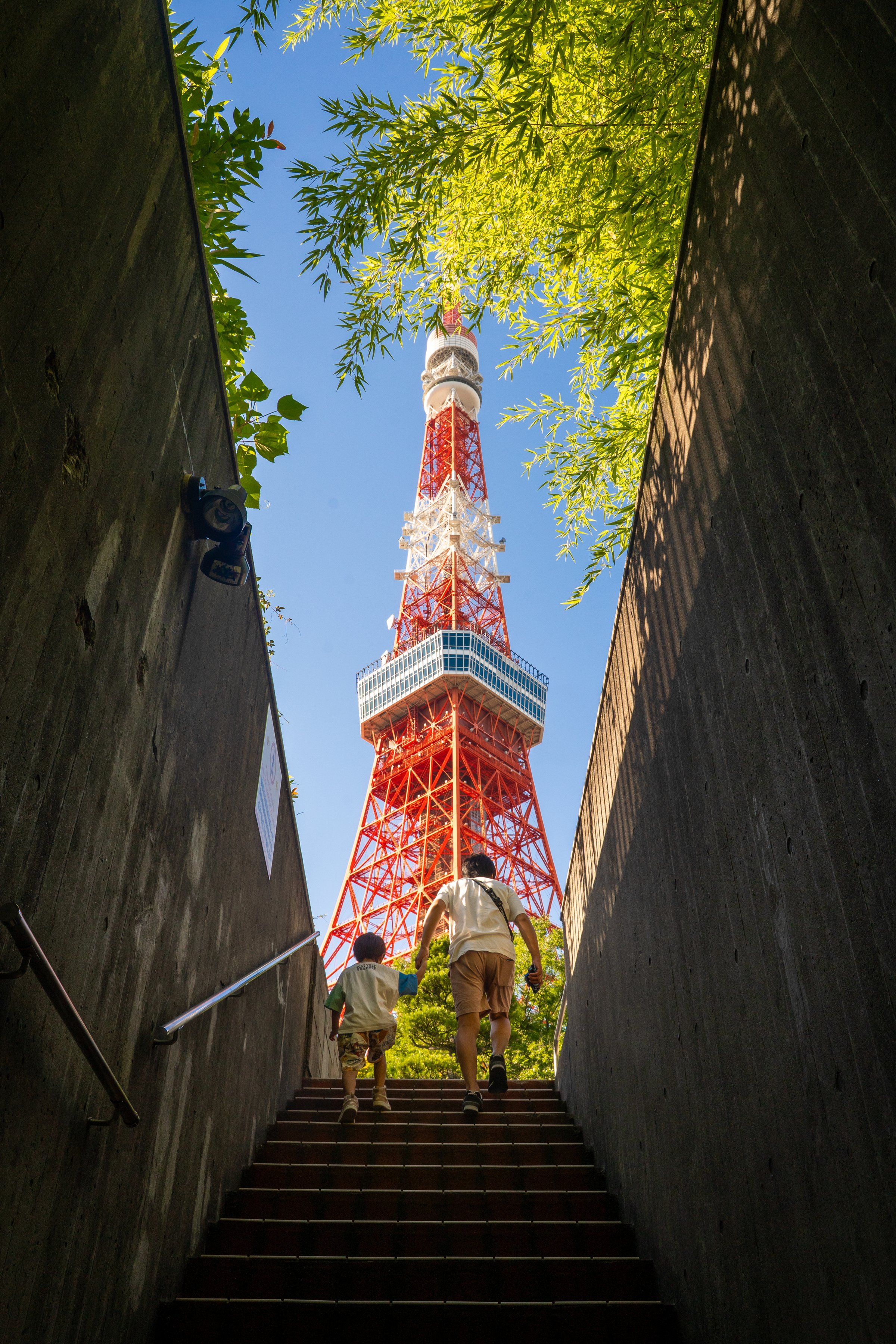 Tokyo Tower viewed from below through concrete staircase with green trees framing